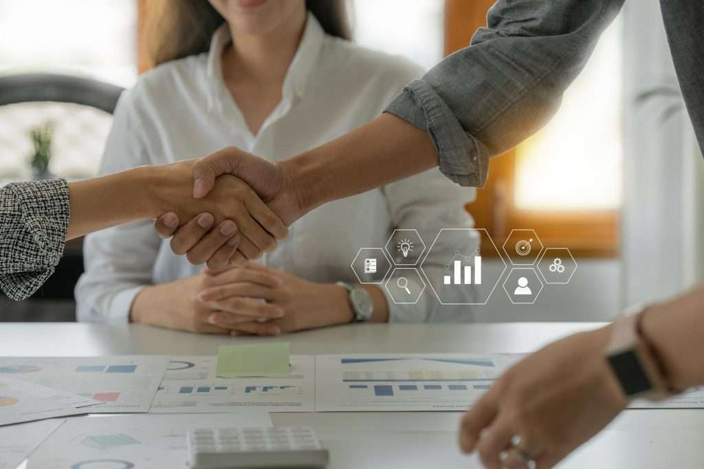 Business people shaking hands over a table, symbolizing partnership and collaboration in a professional setting.